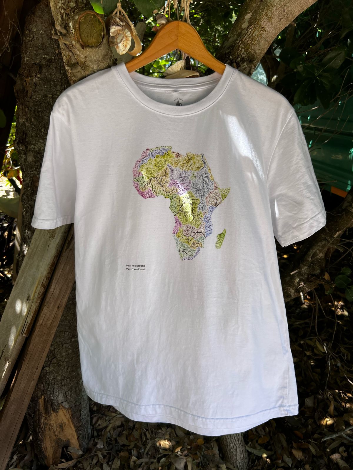 White t-shirt with a colorful Africa map design hanging on a wooden hanger against a natural background.