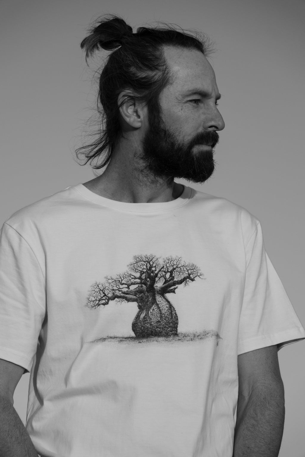 Person wearing a white t-shirt with a baobab tree design on a plain background